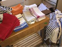 Cloth napkins and aprons on a wooden surface, various colors including red, orange, white, and striped