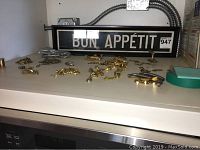 Framed 'BON APPÉTIT' wall art with numerous small door hardware pieces scattered on a white surface.