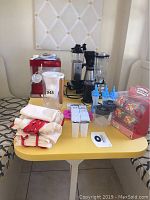 Photo showing red sno cone machine, clear plastic pitcher, blue ice molds, popcorn container, white cloth bags and blender and coffee maker in background.