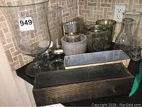 Overview of assorted vases, planters, water can and boxes on black kitchen counter with tiled backsplash.