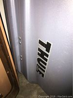 Close-up of Thule brand logo on silver car roof storage box surface.