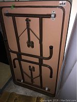 Underside of the folding table showing brown metal folding legs and locking mechanisms.