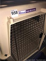 Front view of Petmate Vari Kennel dog crate with metal door and partial label with dimensions 27x27x44 inches.