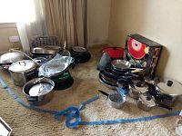 Full lot view of pots, pans, strainers, wok and utensils arranged on carpeted floor showing variety of cookware and accessories.
