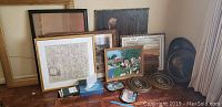 Overall view of multiple framed artworks, decorative trays, and two empty frames on floor