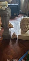 Overview of three stone statues on wooden floor; two larger busts and one small figurine in the center.