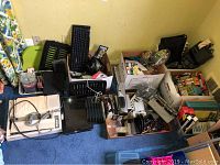 Overview photo of assorted office supplies, electronics, keyboards, and small equipment in boxes and scattered on carpeted floor.