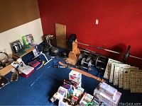 Full lot view showing barbell with weights, dumbbells, belts, blue balance ball, pool noodles, and workout cards laid out on blue carpet against red walls.