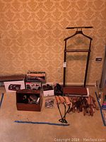 Photo showing wooden valet stand, shoe forms, shoe polisher, boxed shoe shine kit, Easy Spirit shoes, and other shoe care items arranged on carpeted floor against wallpapered background.