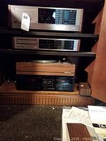 Stacked audio components on wooden shelf: tuner amplifier, CD player, turntable, cassette deck.