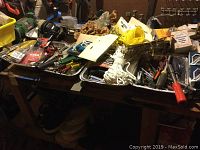 Full view of assorted tools, hardware, hand tools, and equipment on workbench including wrenches, screwdrivers, rope, and small boxes