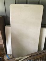 Two white folding plastic tables stacked against wall with visible soiling and dirt marks.