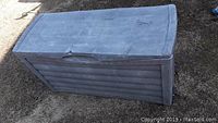 Closed large gray ribbed plastic storage box on outdoor ground.