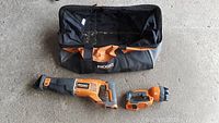 Rigid orange and black sawzall, flashlight and black and orange soft carry bag with Ridgid logo shown laid out on floor.