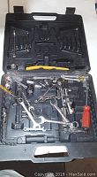 Black plastic tool case open showing assorted wrenches, sockets, yellow brush and red-handled screwdriver.