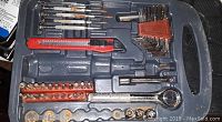 Photo of gray plastic tool case with handle showing Allen wrench set, ratchet socket wrench with sockets, small screwdrivers, and utility cutter inside.
