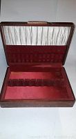 Open wooden silverware case showing red fabric interior with slots for flatware and white fabric inside the lid for additional storage.