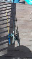 Three fishing rods with reels laid on wooden deck, different colors and sizes