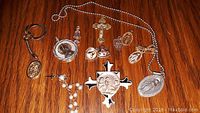 Religious jewelry items including crosses, medallions, rosary beads, and pendants arranged on wooden surface