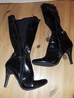 Side view of the pair of black boots showing zipper and heel design on wooden floor.