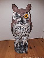 Front view of the owl decoy showing detailed painted feather texture, yellow and black eyes, and base resembling a tree stump.