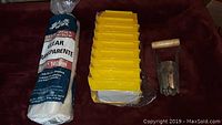 Photo of yellow plastic trays stacked, roll of clear plastic sheeting, and wooden handled metal blade tool resting on a surface.