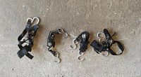 Four black truck ratchet straps with tiedown hooks arranged on concrete floor