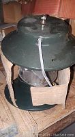 Green metal top and bottom camping lantern with clear glass globe, electrical cord, and bulbs, some wear visible.