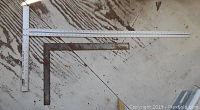 Two metal carpenter squares laid on a wooden surface. One square is approximately 2 feet long, and the other is approximately 44 inches long.