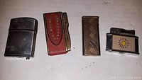 Photo showing four vintage butane lighters laid out side by side on a white surface.