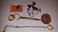 Top view showing all items in the jewelry lot arranged on a white surface including magnifying glass pen, bow brooch, cufflinks, button, two heart lockets, and a small ring in packaging.