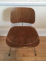 Front and angled view of vintage Eames molded plywood chair showing walnut plywood seat and back with metal legs ending in metal foot caps.