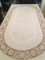 Full view of the oval white linen tablecloth laid on a table, showing the floral lace border and embroidered center area.