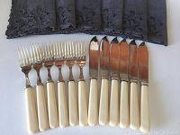 Set of 6 knives and 6 forks with ivory colored handles and silver plated metal, arranged side by side on a fabric surface.