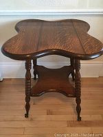 Front side view of the antique oak side table showing the unique tabletop shape, turned legs, and claw feet with glass balls.