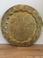 Front view of large brass tray showing intricate floral and leaf embossing and scalloped inner border.