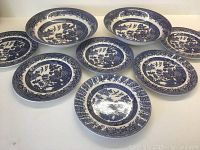 Full set of 2 large Blue Willow pattern serving bowls and 6 smaller dessert plates on white background.