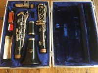 Full clarinet kit laid out in open blue velvet-lined hard case. Shows mouthpiece, upper and lower joints, barrel, bell, and accessories including reed case and cork grease.