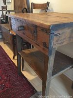 Side angle showing the table's drawer, leg structure and lower shelf with visible wood grain and rustic finish.