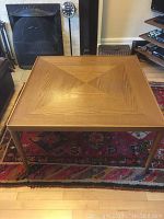 Full view of square wooden coffee table showing the inlaid mitred top and tapered legs on a red patterned rug.