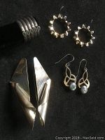 Photo showing all four items: long twisted slab earrings, gear-inspired earrings, vintage earrings with stones, and small ring with stones, arranged on black background