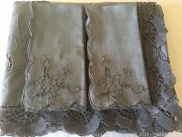 Folded tablecloth showing steel blue/grey linen with embroidery and lace trim.