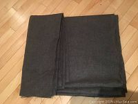 Folded charcoal grey upholstery fabric displayed on a wooden floor showing length and width.