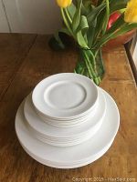 Stack of three sizes of white Royal Worcester china plates on wooden surface with flowers in background