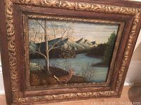 Full view of the framed oil painting depicting a deer near trees by a river with mountains and a boat in background.
