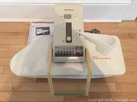 Full view of Singer Magic Steam Press MSP-8 on ironing pad with attached water reservoir and user manual beneath.