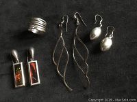 Four pairs of earrings and one ring displayed on dark cloth, showing the variety in shapes and styles including amber rectangular earrings and curved wire earrings.