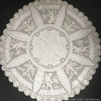 Full view of the round antique tablecloth showing scalloped lace edge, embroidered floral motifs, and cherub lace panels.