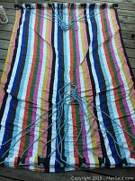 Photo of the hammock laid flat showing its striped cloth fabric, wooden spreader bars, and attached hanging ropes.