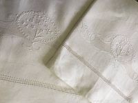 Close-up image of matching top sheet and pillow sham folded together showing hand embroidered floral design and decorative hemstitching.